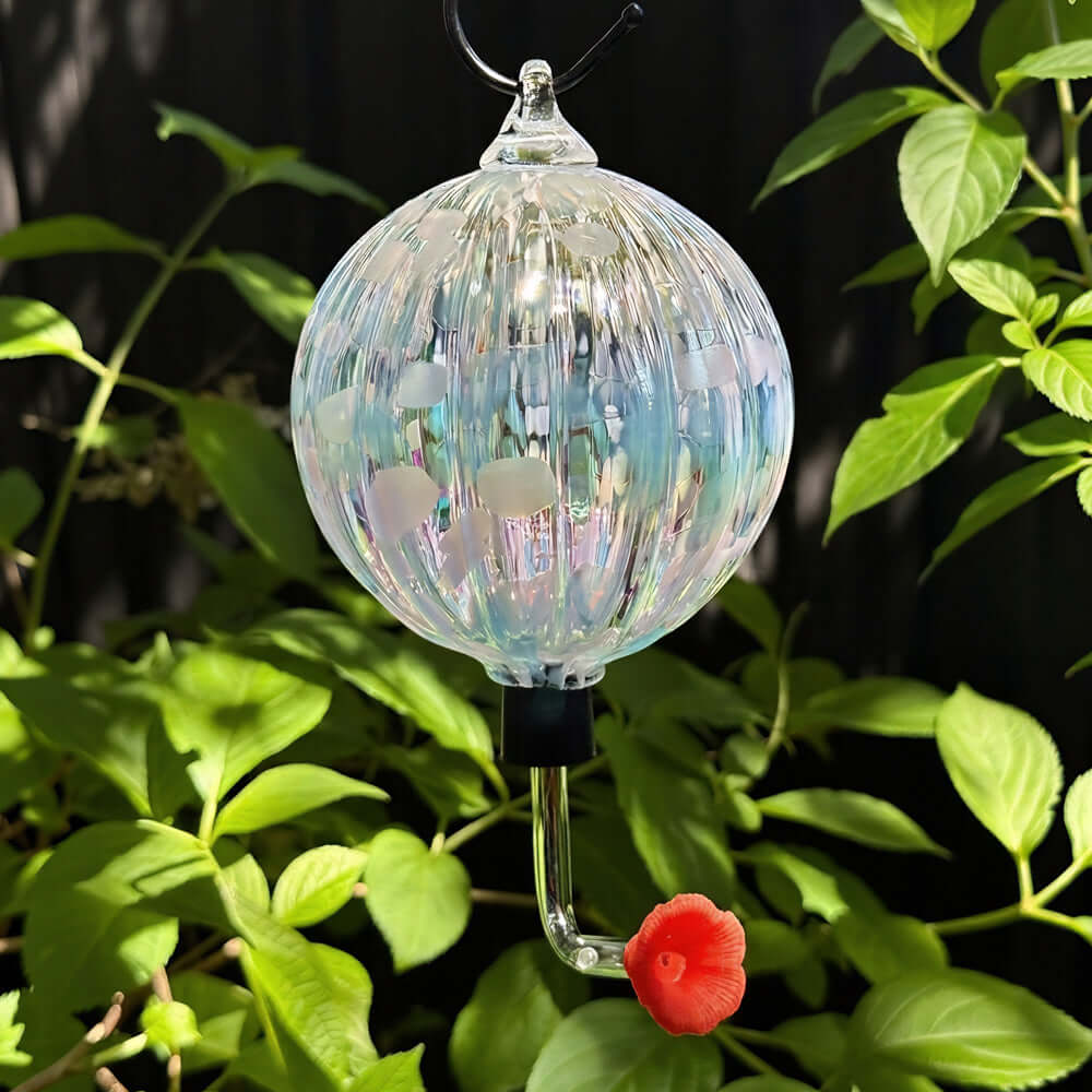 Colorful Baby Blue Eyes glass ornament with a red flower serving as a bird feeder, surrounded by green leaves.